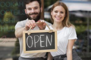 Business owners achieving stable franchise growth as they proudly hold an 'Open' sign at their new franchise location.