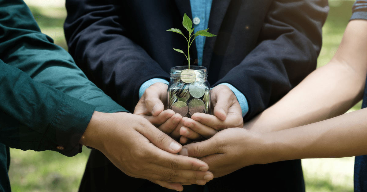 Business professionals holding a glass jar with coins and a growing plant, symbolizing sustainable franchises and financial growth.