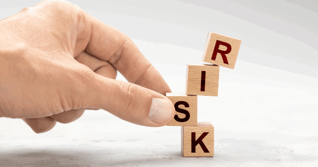 Stacked wooden blocks spelling “RISK” tilting as a hand steadies them, symbolizing franchise risk management.