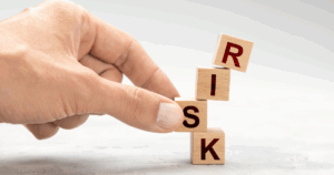 Stacked wooden blocks spelling “RISK” tilting as a hand steadies them, symbolizing franchise risk management.